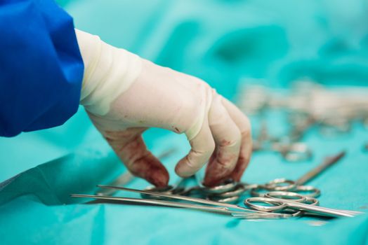 Surgeon hand picking up an instrument from tray of surgical instruments