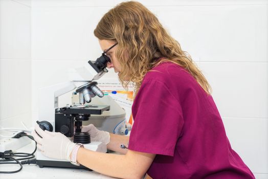 Young laboratory assistant looking through a microscope