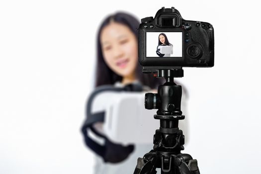 Focus on live view on camera on tripod, teenage girl  using VR goggles image on back screen with blurred scene in background. Teenage vlogger livestreaming show concept