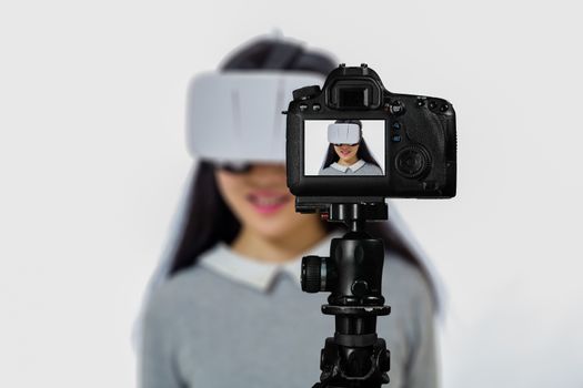 Focus on live view on camera on tripod, teenage girl  using VR goggles image on back screen with blurred scene in background. Teenage vlogger livestreaming show concept