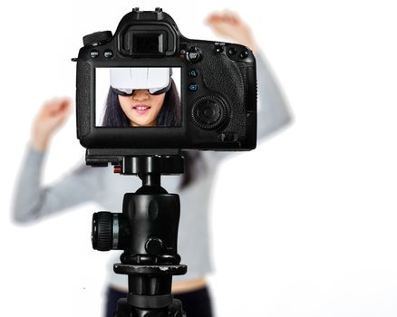 Focus on live view on camera on tripod, teenage girl  using VR goggles image on back screen with blurred scene in background. Teenage vlogger livestreaming show concept