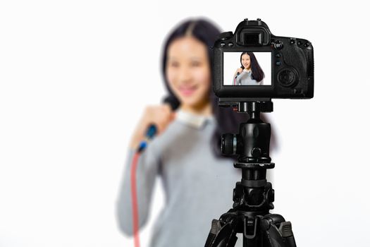 Focus on live view on camera on tripod, teenage girl  singing with microphone image on back screen with blurred scene in background. Teenage vlogger livestreaming show concept