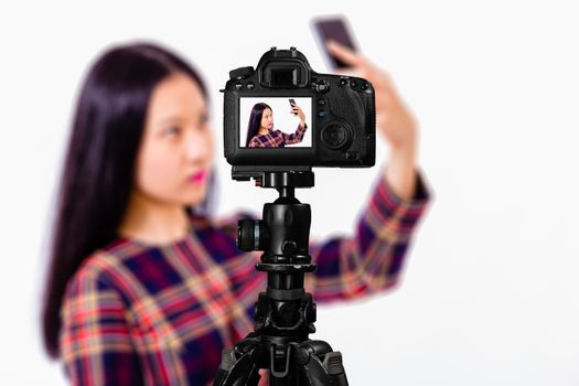 Focus on live view on camera on tripod, teenage girl  taking selfie image on back screen with blurred scene in background. Teenage vlogger livestreaming show concept