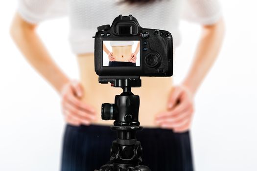 Focus on live view on camera on tripod, teenage girl  showing waistline from diet image on back screen with blurred scene in background. Teenage vlogger livestreaming show concept