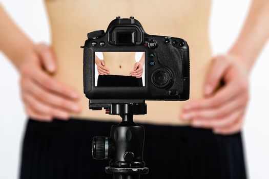 Focus on live view on camera on tripod, teenage girl  showing waistline from diet image on back screen with blurred scene in background. Teenage vlogger livestreaming show concept