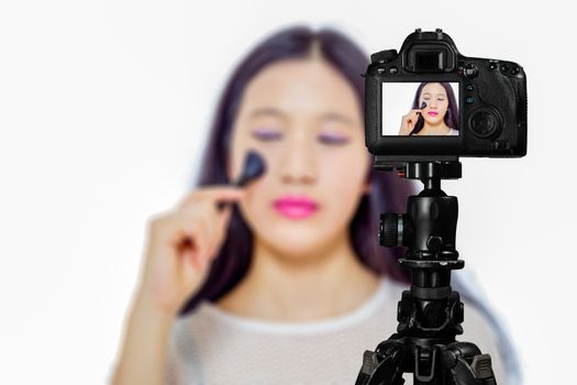 Focus on live view on camera on tripod, teenage girl  using cosmetics image on back screen with blurred scene in background. Teenage vlogger livestreaming show concept