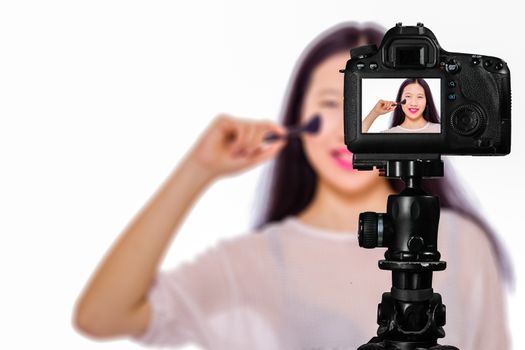 Focus on live view on camera on tripod, teenage girl  using cosmetics image on back screen with blurred scene in background. Teenage vlogger livestreaming show concept