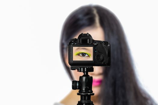 Focus on live view on camera on tripod, teenage girl  makeup beauty shoot image on back screen with blurred scene in background. Teenage vlogger livestreaming show concept