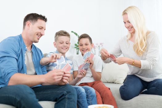 Happy young family playing card game on living room sofa at home. Spending quality leisure time with children and family concept. Cards are generic and debranded.