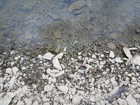 broken grey rocks and water at shore of river or lake or pond