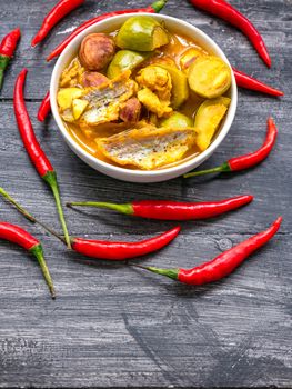 Southern Thai Spicy Sour Yellow Curry with dried fish and Thai eggplant in white bowl and red chilli on black painted wooden background.