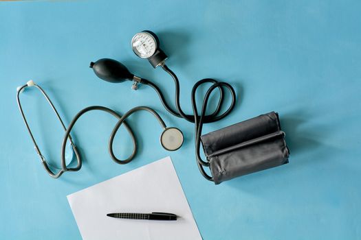 White sheet paper with black pen and phonendoscope stethoscope, sphygmomanometer on blue background with copy space for text. Medicine consept.