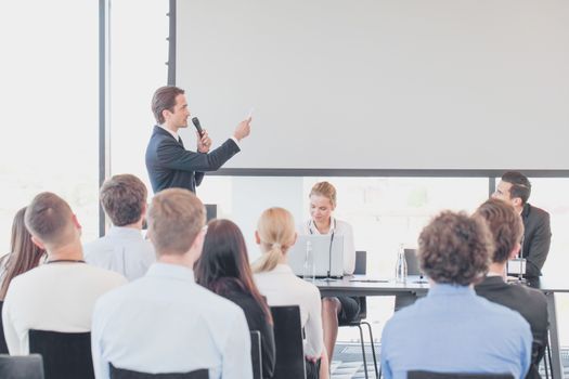 Speaker at business conference near white screen and audience