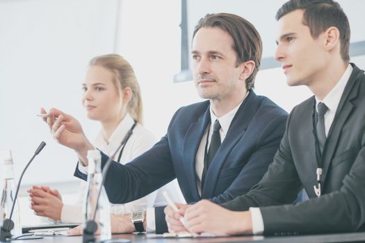 Group of speakers at business meeting at the table with microphones