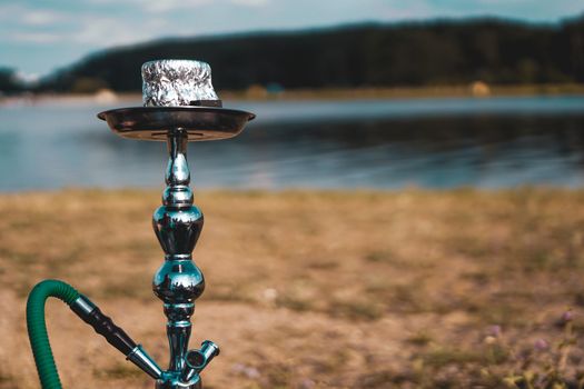 Summer vacation, activity. environment, travel and hookah smoking concept. Hookah bowl stands in nature by the river close up