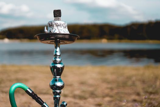 Summer vacation, activity. environment, travel and hookah smoking concept. Hookah bowl stands in nature by the river close up