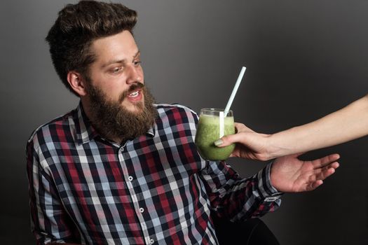 Young Man looks incredulously at woman giving him healthy eating green spinach smoothie