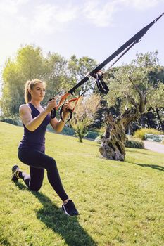 vertical photo of an attractive young woman training fitness with suspension straps, she is outdoors during functional workout