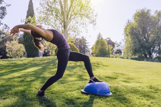 healthy young woman doing stretching yoga workout on the grass on a sunny day, she is outdoors in a park at the morning