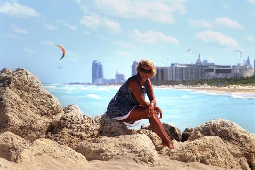 The girl sits on a stone against the backdrop of Miami Beach