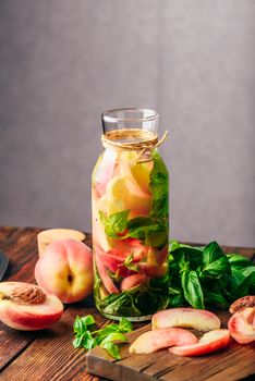Bottle of Detox Water with Sliced Peach and Basil Leaves. Knife and Ingredients on Cutting Board. Vertical Orientation.