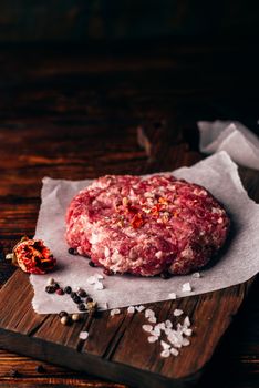 Raw Round Patty with Peppercorns, Salt and Chili Pepper on Wax Paper for Burger.