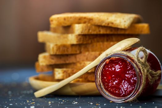 Strawberry jam bottle and whole wheat bread are stacked on a black background. Concept of breakfast and healthy food.