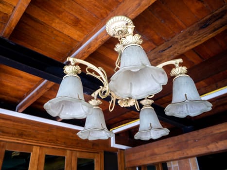 beautiful vintage interior background of a lighted retro chandelier hanging on a wooden ceiling, decorated lamp with flowers