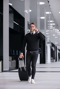 Man walking with wheeled bag at airport terminal and talking on phone