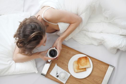 Beautiful young woman having breakfast in bed