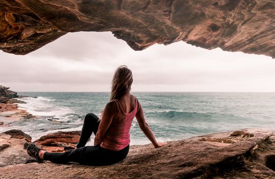 Woman in active wear relaxing in a cave overhang on rocks by the ocean