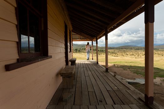 Woman standing on verandah of rustic timber homestead with scenic views in the snowy high plains. A storm is brewing out over the ranges