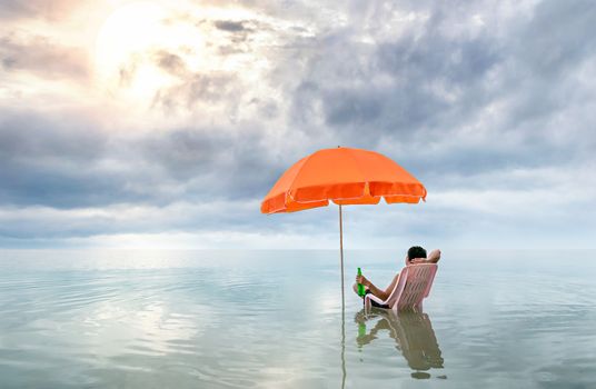 Happy man sitting on pink lounge chairs with  sun umbrella in a sea
