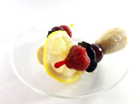 Dish for gourmet. Healthy food. Vegetarian foods on transparent plate. Berries and fruits. Lemon and cherry for a snack. Photo for modern design. Canapes made from bananas, strawberries and cherries.