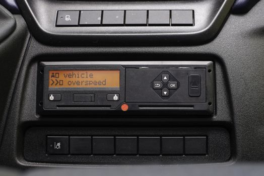 Digital tachograph display reads Vehicle Overspeed. No personal data. Tachograph in a van.