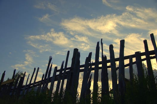 A look at the cloudy evening sky through an old wooden fence.