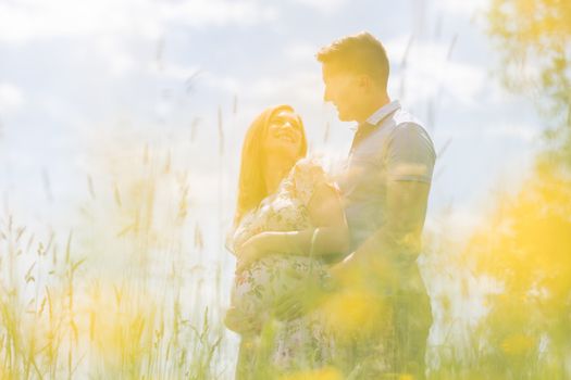 Young happy pregnant couple hugging in nature. Concept of love, relationship, care, marriage, family creation, pregnancy, parenting