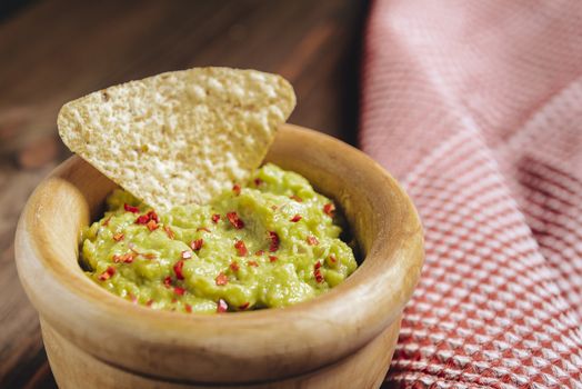 homemade guacamole with nachos in a wood bowl and a kitchen rag on a wooden table, typical mexican healthy vegan cuisine