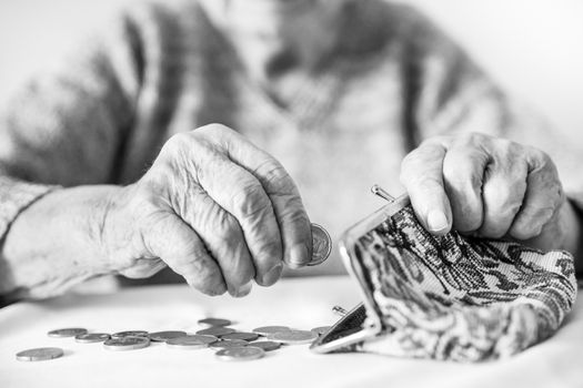 Detailed closeup photo of elderly 96 years old womans hands counting remaining coins from pension in her wallet after paying bills. Unsustainability of social transfers and pension system.