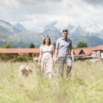 Young happy pregnant couple holding hands walking it's Golden retriever dog outdoors at countryside. Concept of love, relationship, care, devotion, marriage, family creation, pregnancy, parenting