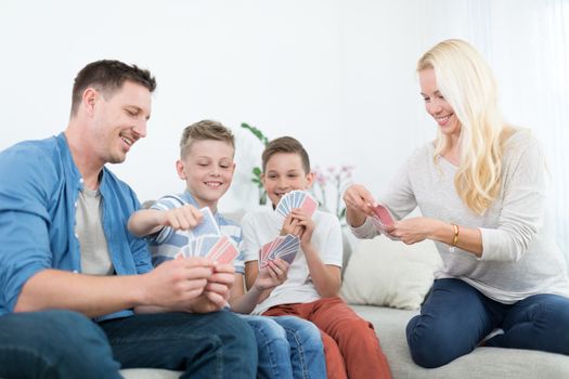 Happy young family playing card game on living room sofa at home. Spending quality leisure time with children and family concept. Cards are generic and debranded.