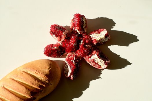 Garnet. Bread. Bread long loaf and ripe red juicy pomegranate. Grains pomegranate fruit. Pomegranate cut in the form of a star. Lonely fruit on a light background. Hard daylight.