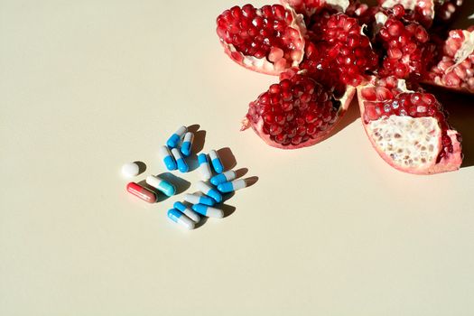 Garnet. Tablets and capsules, pills. The concept of a healthy life. Ripe red juicy pomegranate and pills, capsules, pills lying separately on a white background. Grains pomegranate fruit.