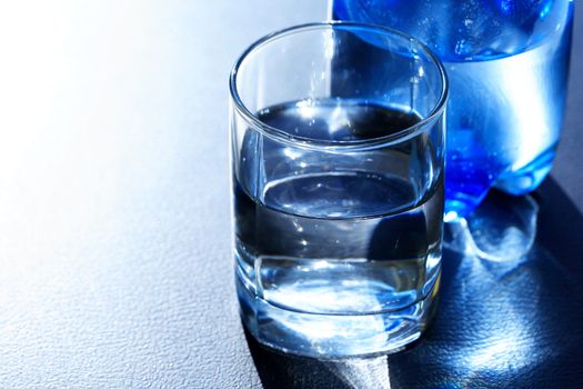 Closeup of glass of mineral water near blue plastic bottle