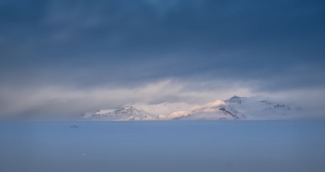 Focssed morning sunshine on a mounting range, winter day in Iceland with overcast sky and snow-covered land
