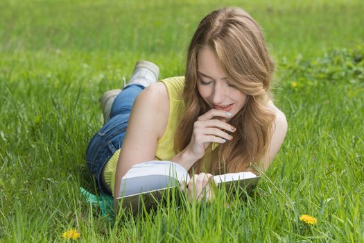 Pretty girl laying on the grass and reading a book in spring park and smiling