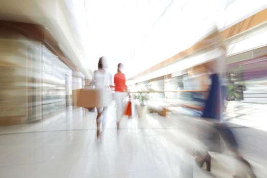 Abstract defocused motion blur background of girls walking fast in shopping mall with bags