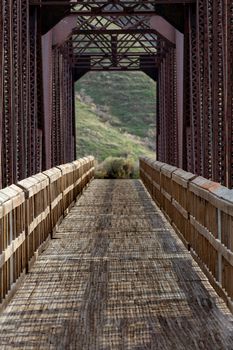 showing a path leading to a grassy hill by going through a wooden bridge