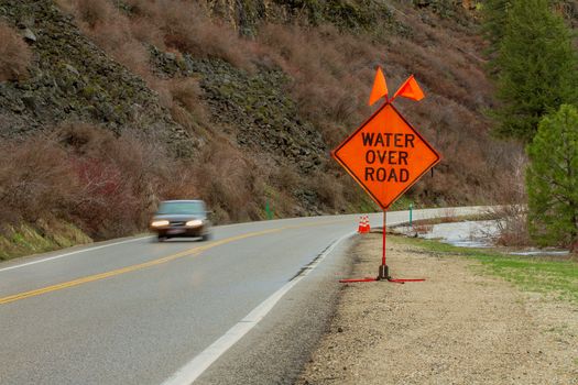 car driving by a sign indicating that there is water on the road