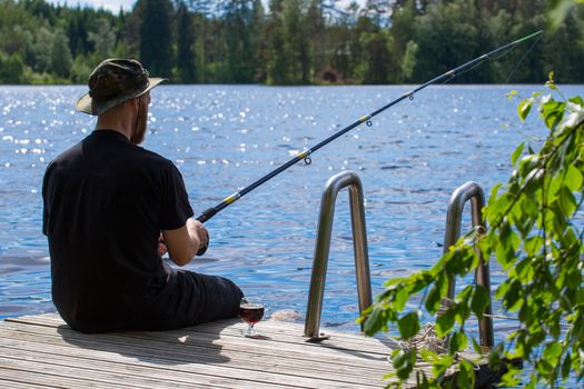 Mature man fishing from wooden pier near cottage on lake in Finland at summer